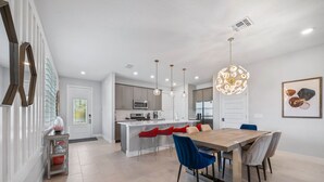 A modern kitchen with a central island, pendant lighting, and a dining area with a wooden table and chairs. - Eagle Trace Monroe: Water Park, Golf View, Near Disney (Kissimmee)