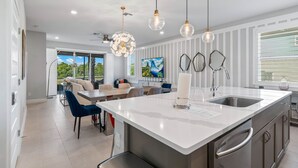 A modern kitchen with a large island, pendant lights, and a view of the outdoors. - Eagle Trace Monroe: Water Park, Golf View, Near Disney (Kissimmee)