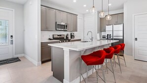 A modern kitchen with a central island, stainless steel appliances, and red bar stools. - Eagle Trace Monroe: Water Park, Golf View, Near Disney (Kissimmee)