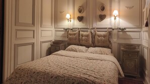 A bedroom with a large bed, two nightstands, a dresser, and decorative wall sconces.