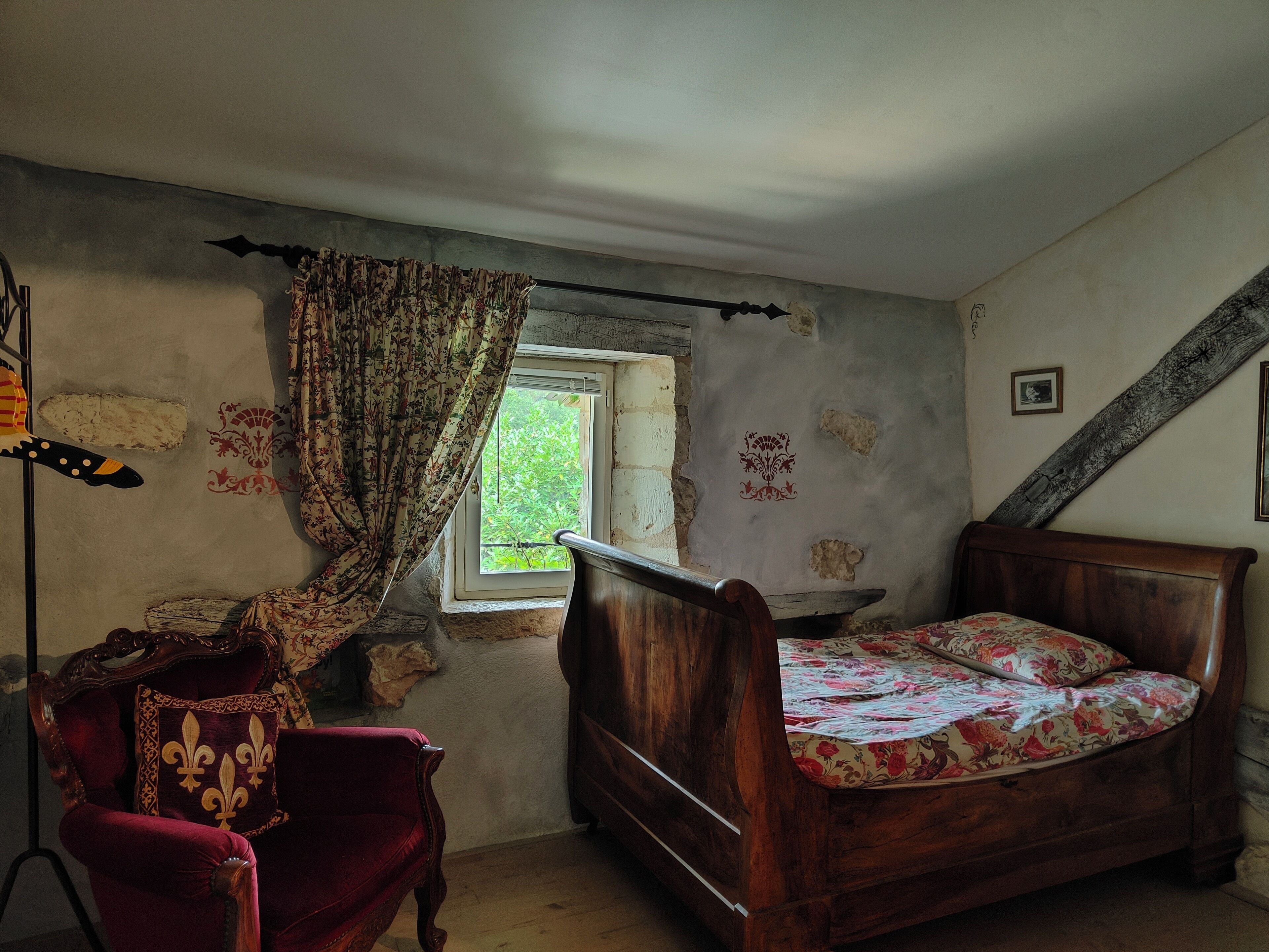 Un dormitorio con una cama de madera, una silla roja, una ventana con cortinas y un techo inclinado.