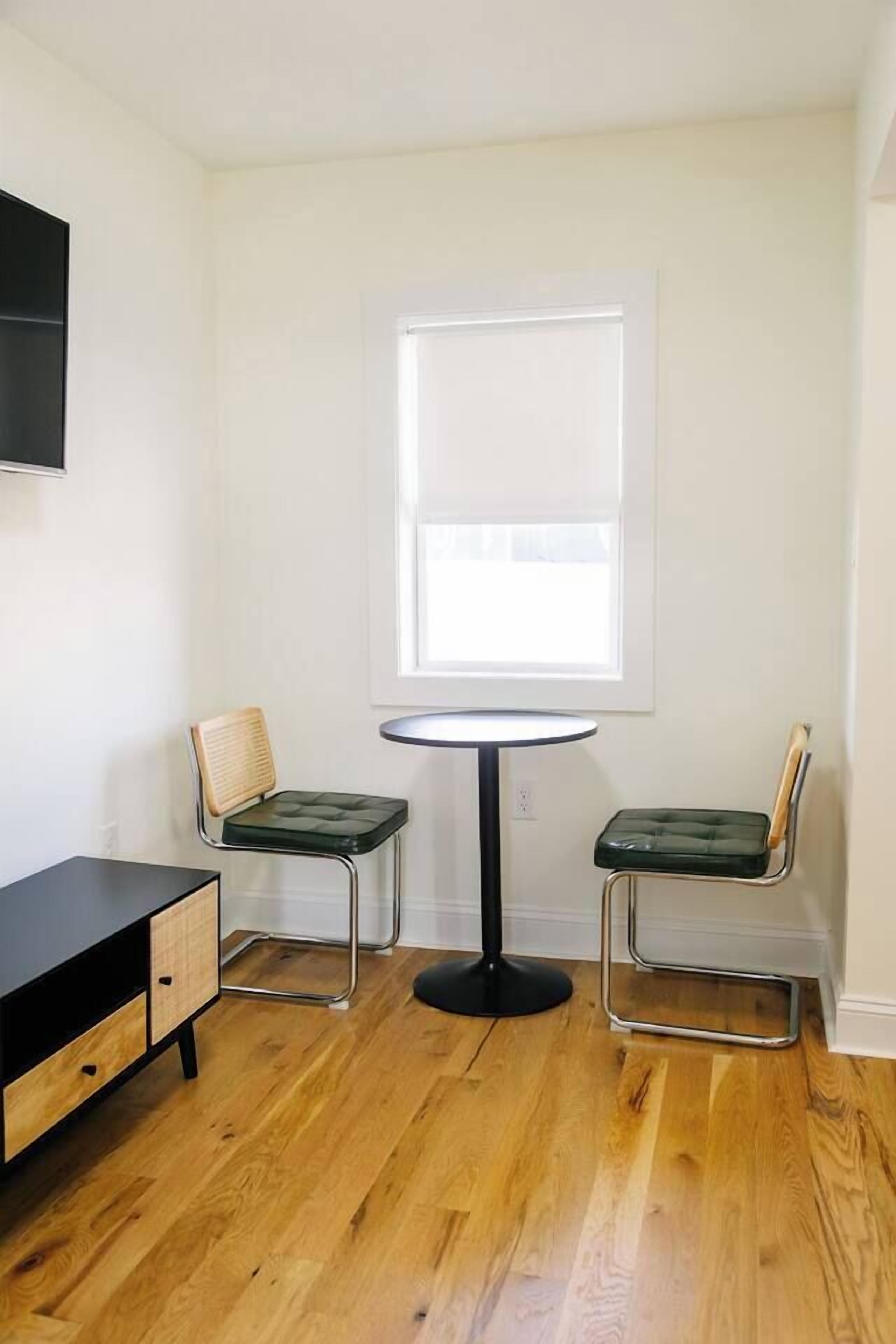 Une petite pièce avec une table ronde et deux chaises, un meuble noir et une fenêtre.