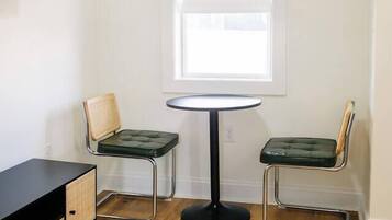 Une petite pièce avec une table ronde et deux chaises, un meuble noir et une fenêtre.