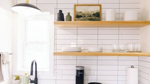 Et køkken med hvide metrofliser, en stålvask, en sort elkedel og hylder med service og glas.