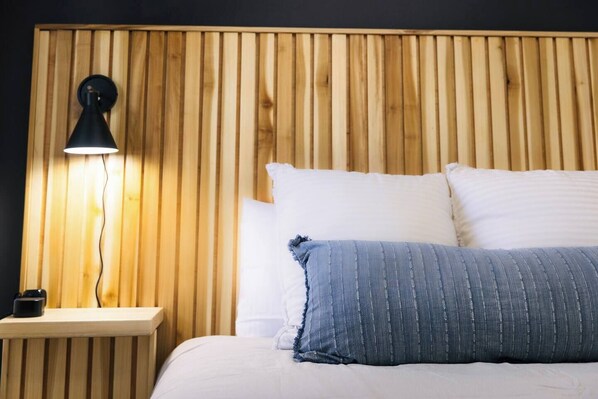 Una cama con almohadas a rayas blancas y azules, un cabecero de madera y una mesita de noche con una lámpara.
