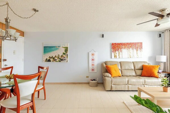 A living room with a beige sofa, a dining table with chairs, a ceiling fan, and a beach-themed wall art. - Beachfront Condo Isla Verde Avenue Marbella Este!! Right on the Beach!!⛱️
(Isla Verde)
