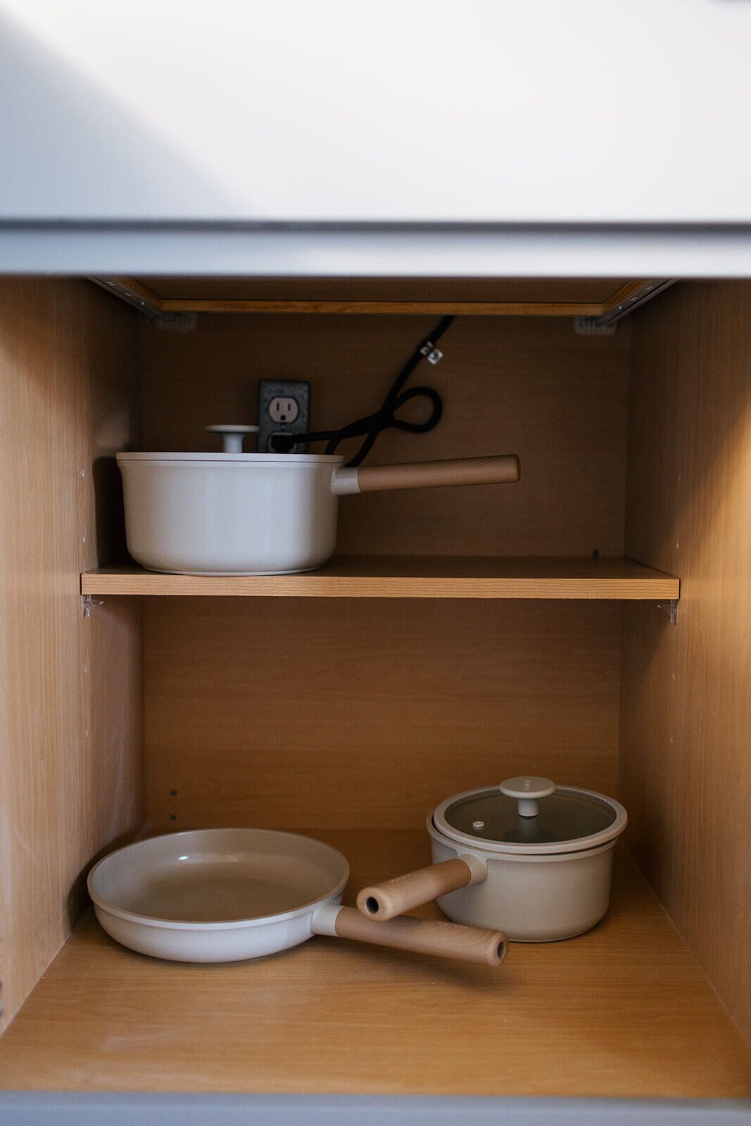 Une cuisine avec des meubles de rangement en bois, une casserole blanche sur l’étagère supérieure, et une poêle et une autre casserole sur l’étagère inférieure.