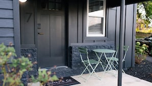 A dark gray building with a door, a window, and a small outdoor seating area with two chairs and a table. - Tiny Home with Loft, WI-FI + Free Parking! (Chambersburg)