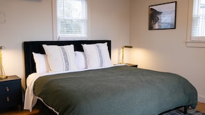 A neatly made bed with a green blanket, white pillows, and a black headboard in a room with wooden flooring and two bedside lamps.