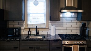 A modern kitchen with a gas stove, a microwave, a sink, and a window with blinds.