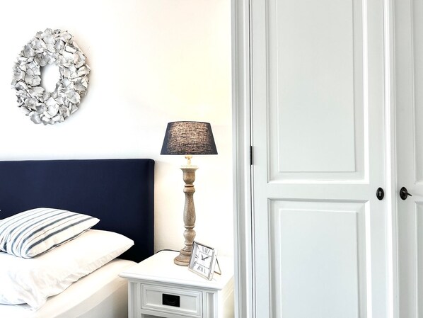 Une chambre à coucher avec un lit, une table de chevet, une lampe, un élément de décoration murale et une porte.