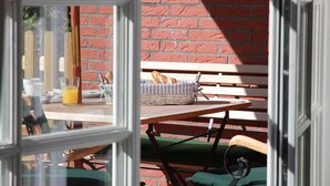 Una mesa con una cesta de pan, un vaso de jugo de naranja y una taza, frente a un muro de ladrillo.