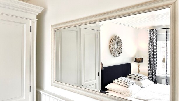 Un dormitorio con un espejo grande, una cama con ropa de cama a rayas, un reloj de pared y una guirnalda decorativa.