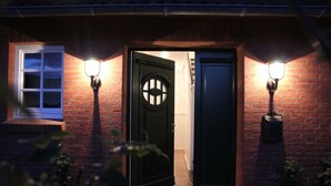 Una casa de ladrillo con una puerta oscura, dos luces fijadas a la pared y una ventana con marco blanco.