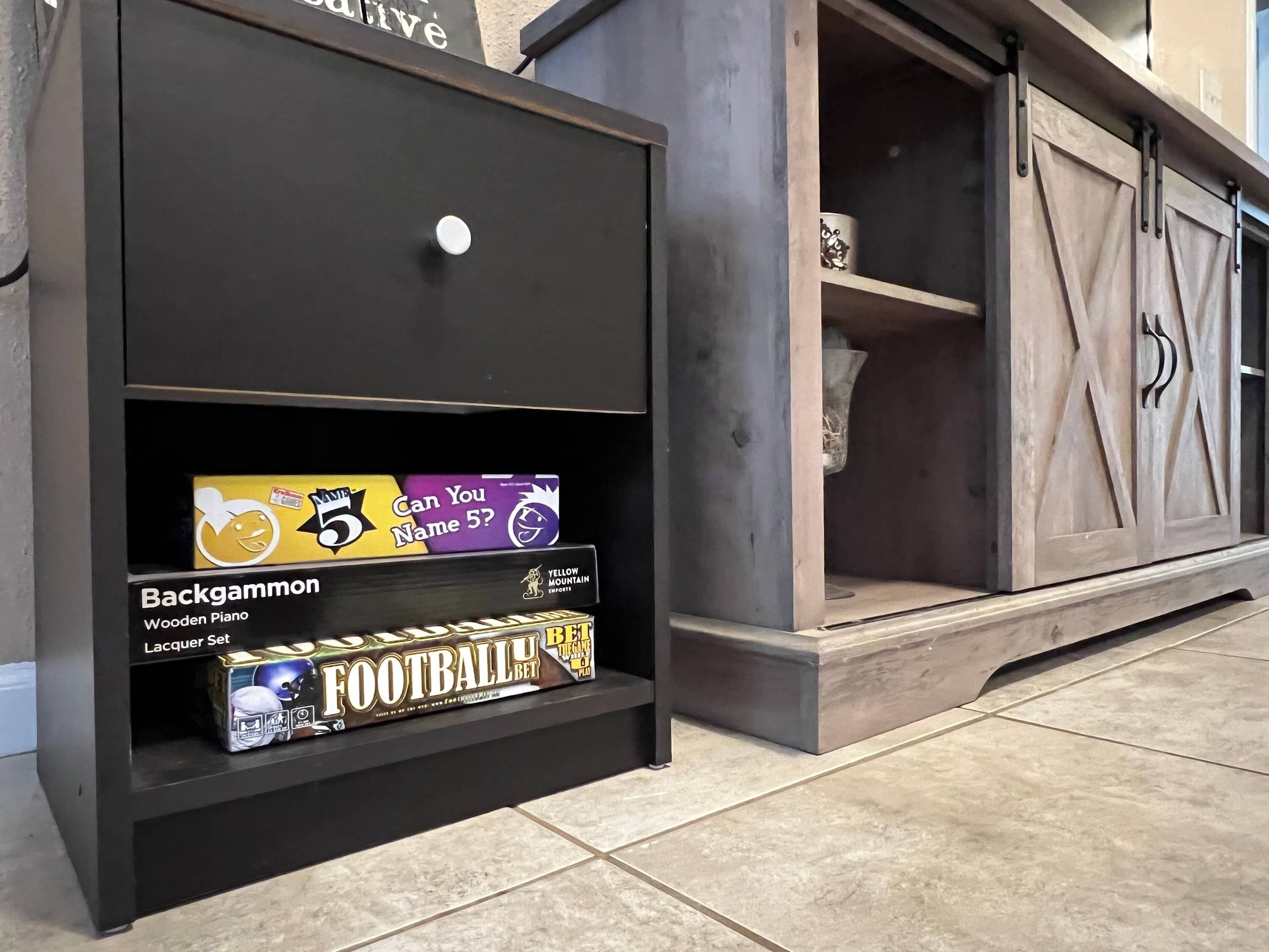 Een zwart schap met een witte knop, waarop onder andere een houten piano, een wedden op voetbal boek en een pot staan.