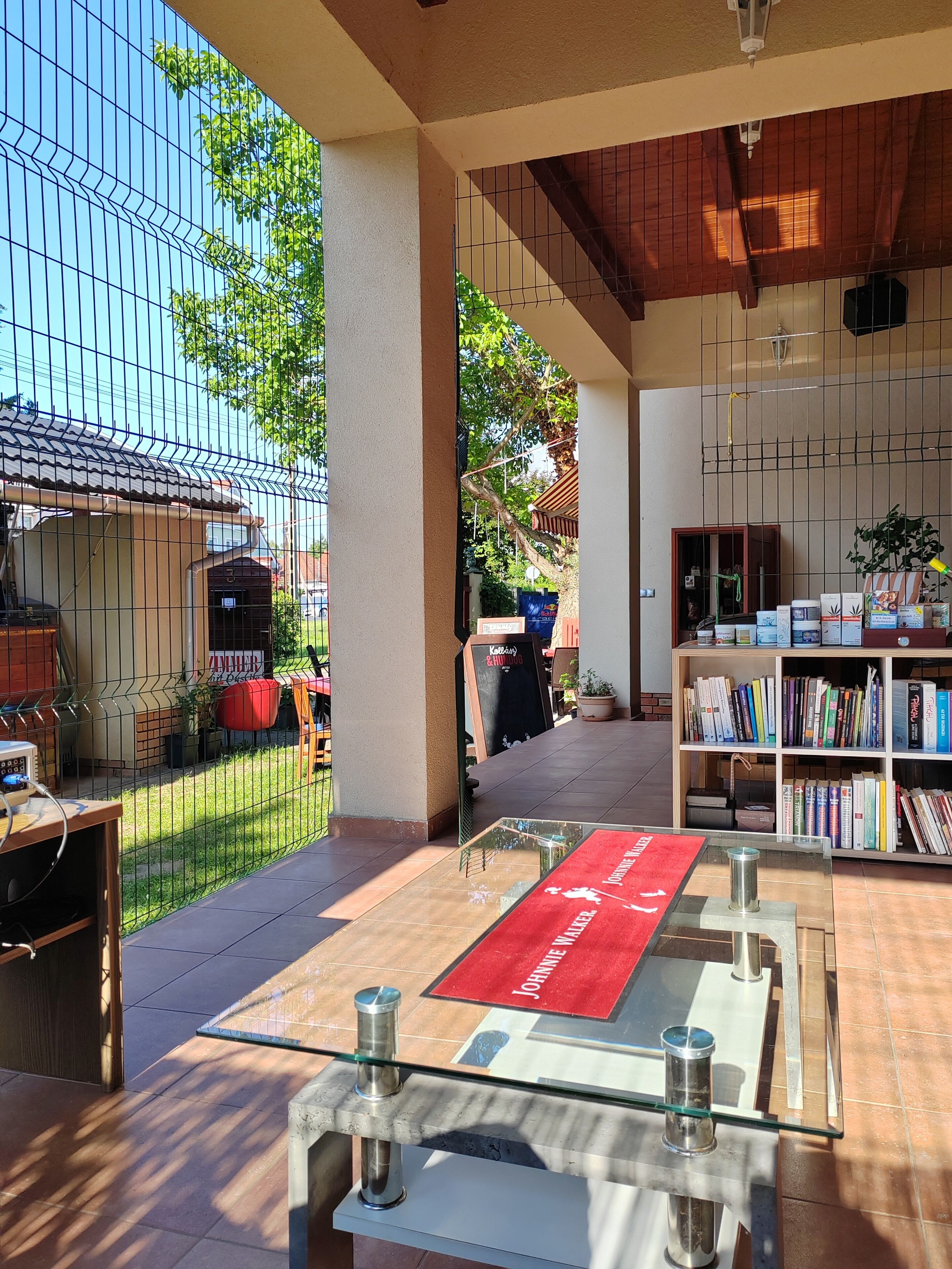 Un espace extérieur aménagé avec une table en verre, des chaises en métal et un tapis rouge.