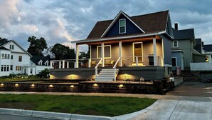 A two-story house with a porch and a stone retaining wall. - Pristine Home Perfect for Family Bay Views Luxe Chef’s Kitchen Ludington Park (Escanaba)