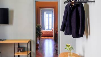 A room with a bed, a TV, a table with a radio, and a hanging coat rack.