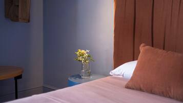 A bedroom with a bed, a nightstand with a vase of flowers, a wooden chair, and a brown headboard.