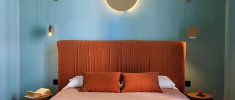A bedroom with a large bed, two pillows, a bedside table with a book, and a wall-mounted light fixture.