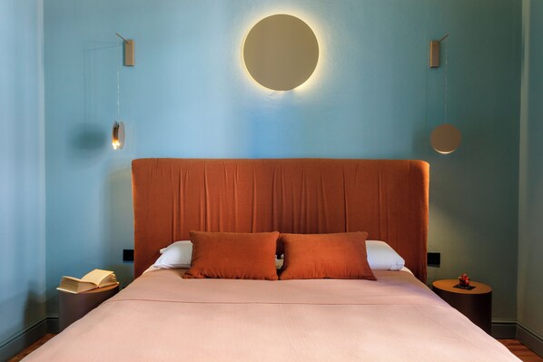 A bedroom with a large bed, two pillows, a bedside table with a book, and a wall-mounted light fixture.