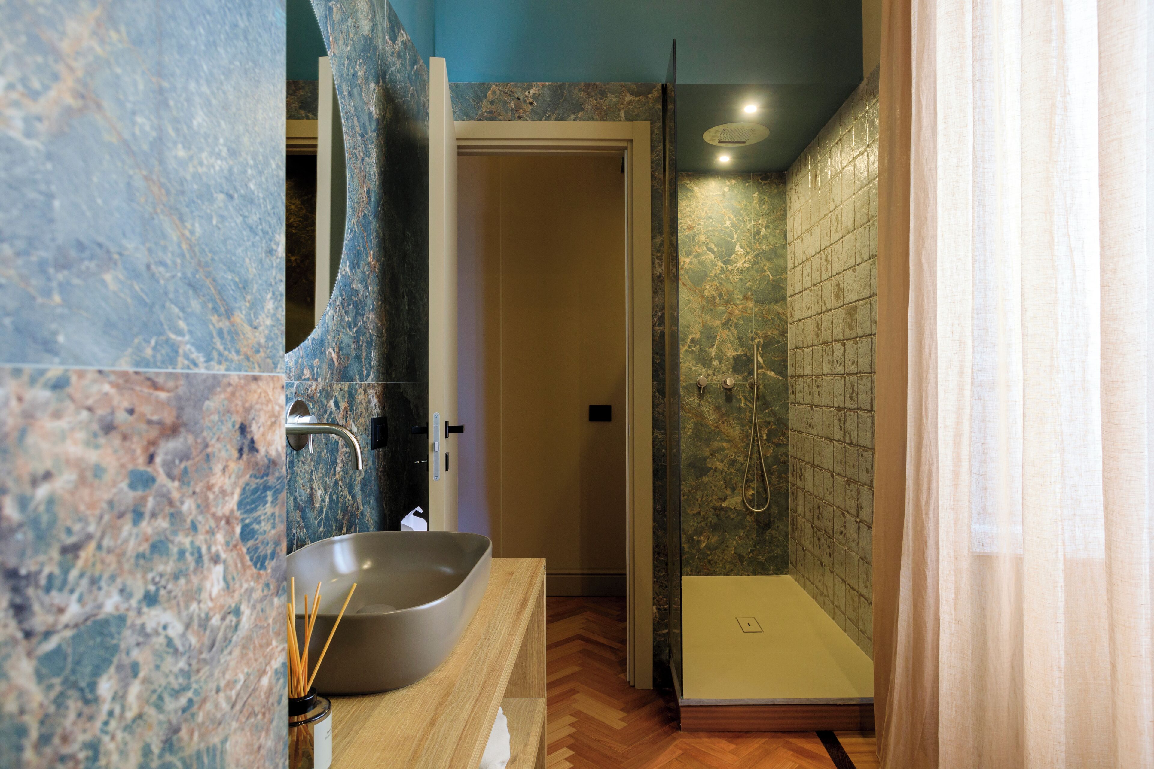 Un baño con lavamanos de mármol, ducha y suelo de madera.
