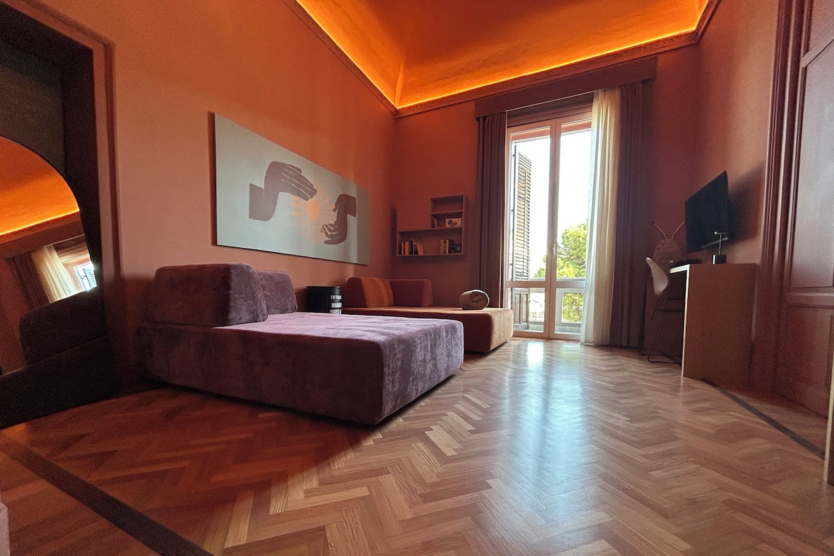 A modern bedroom with a large bed, a sofa, a desk, and a TV.