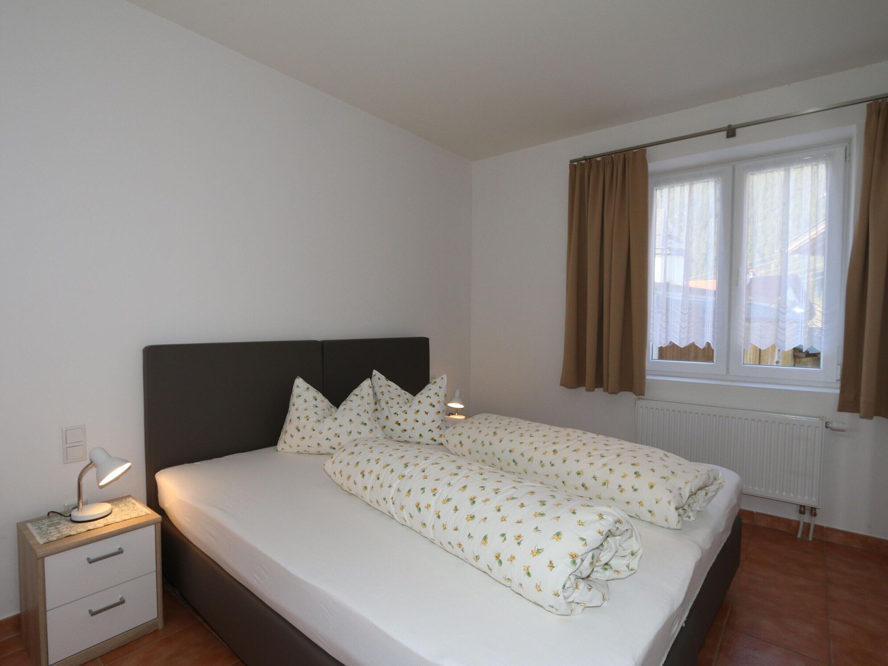 A bedroom with a bed, nightstand, and window with curtains.