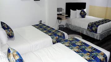 A hotel room with two single beds, each with a blue and gold patterned bedspread, white pillows, and a small bedside table with a lamp and a phone.