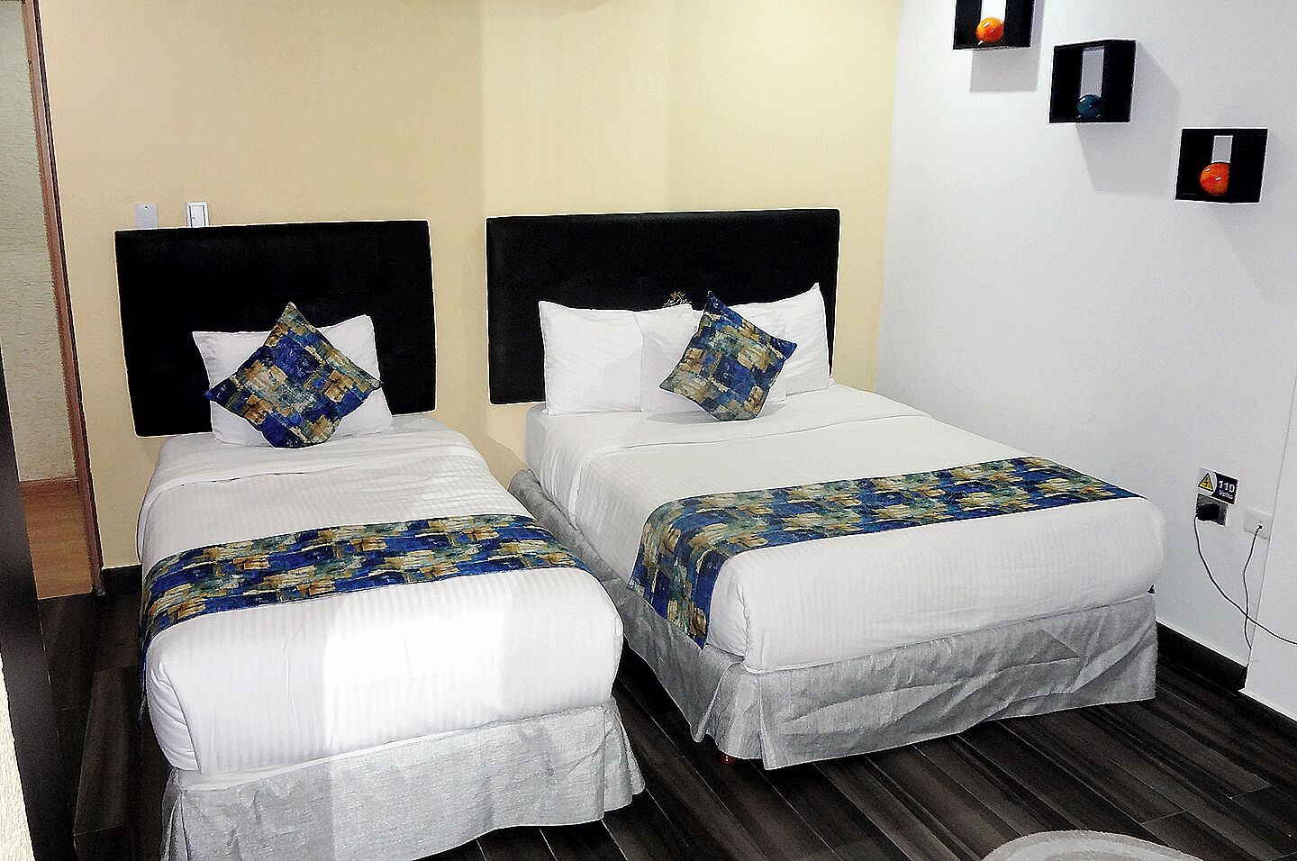 Two single beds with black headboards, white bedding, and patterned throw pillows.