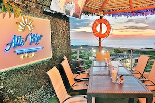 Restaurante con terraza al aire libre con vistas al mar, con un letrero de neón, un flotador salvavidas y un techo de paja.
