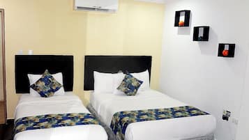 Une chambre d’hôtel avec deux lits, chacun doté d’une tête de lit noire et de draps blancs. Un appareil de climatisation est fixé au mur au-dessus des lits.