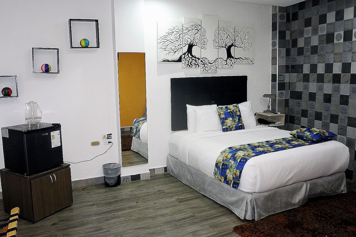 A bedroom with a bed, a nightstand, a mirror, a dresser, and a wall with artwork.