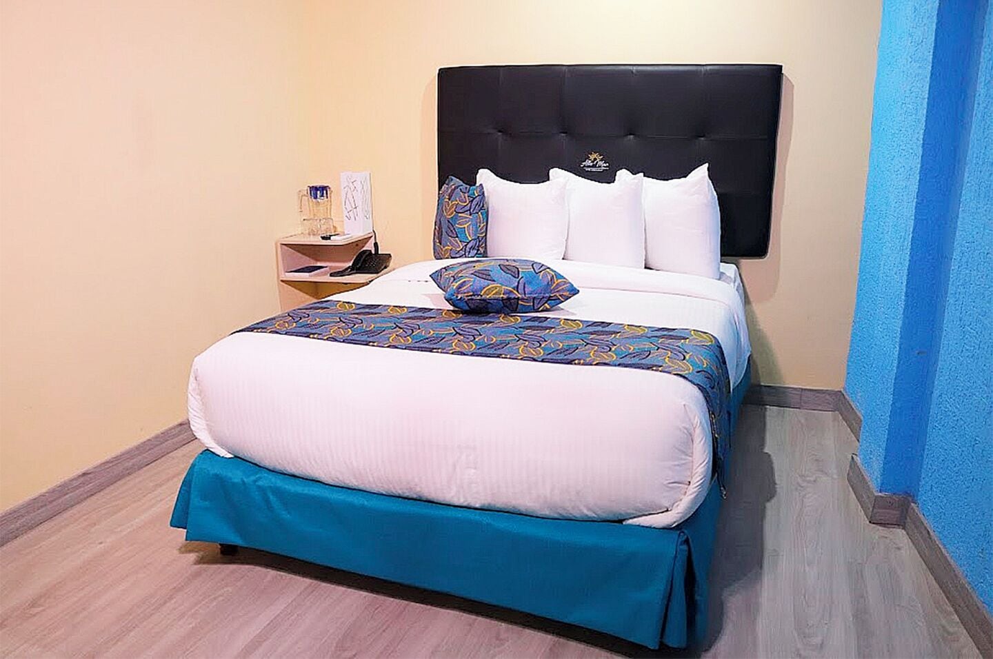 A bed with a black headboard, white and blue patterned bedspread, and matching pillows.