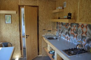 Compact kitchen with a sink, gas stove, and decorative backsplash, featuring ample storage and a convenient chair.