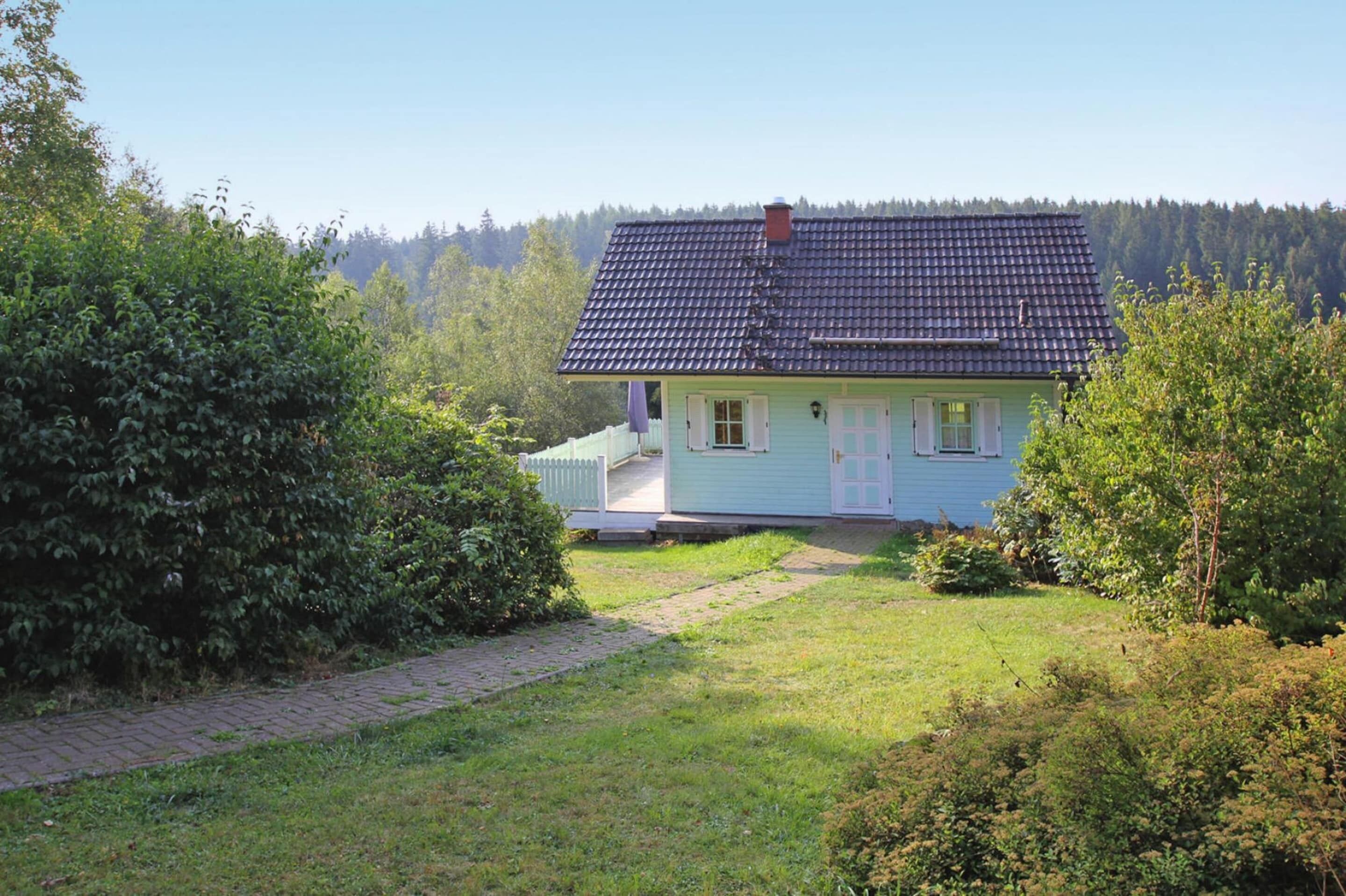 A single-story house with a dark tiled roof, a light blue exterior, and a white picket fence.
