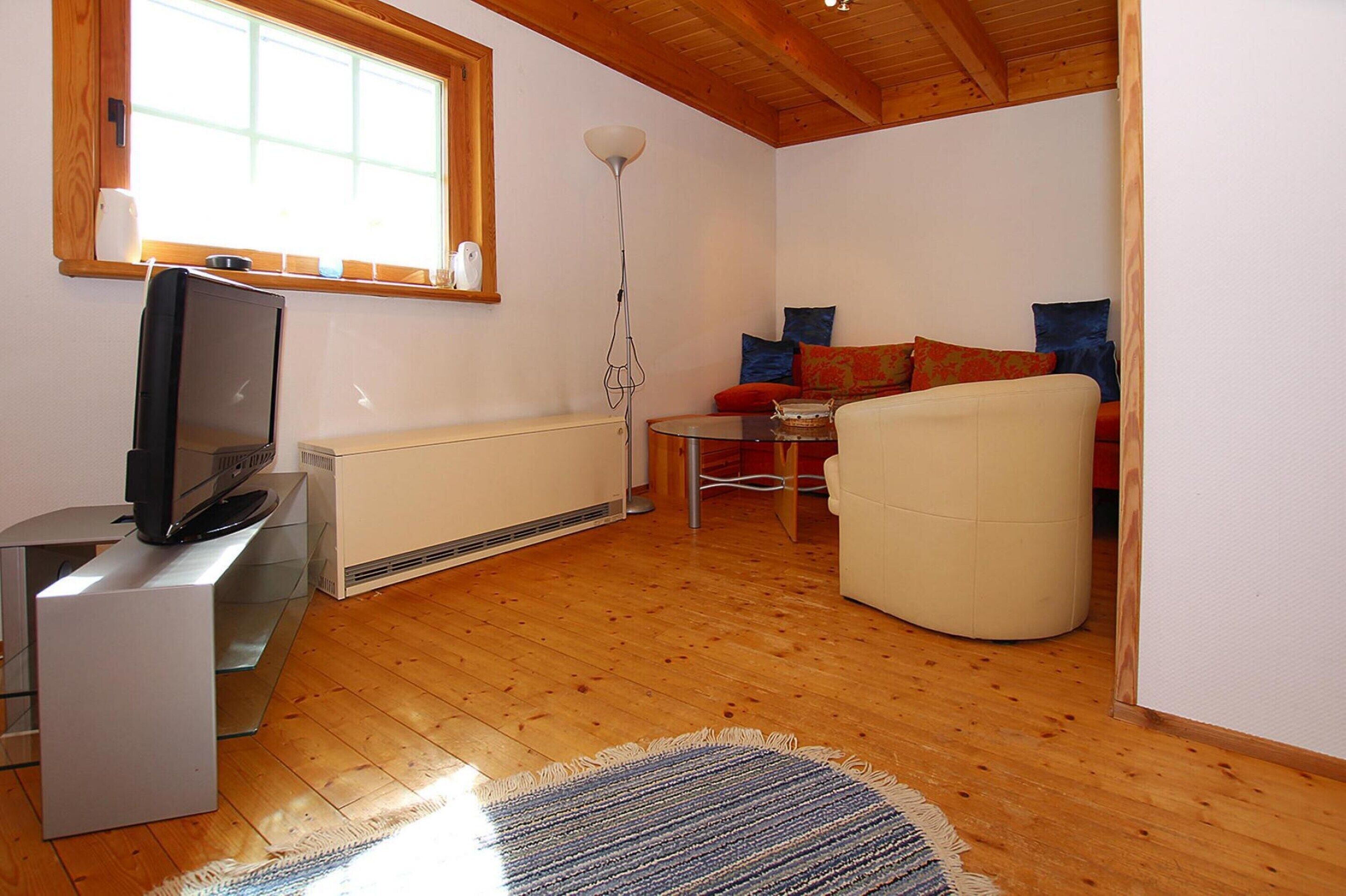 Uma sala de estar com televisão sobre um suporte, um sofá, uma mesa de centro e um abajur.