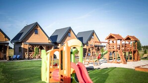 Ein Spielplatz mit Rutsche, Schaukeln und Klettergerüsten vor einer Häuserreihe mit schrägen Dächern.