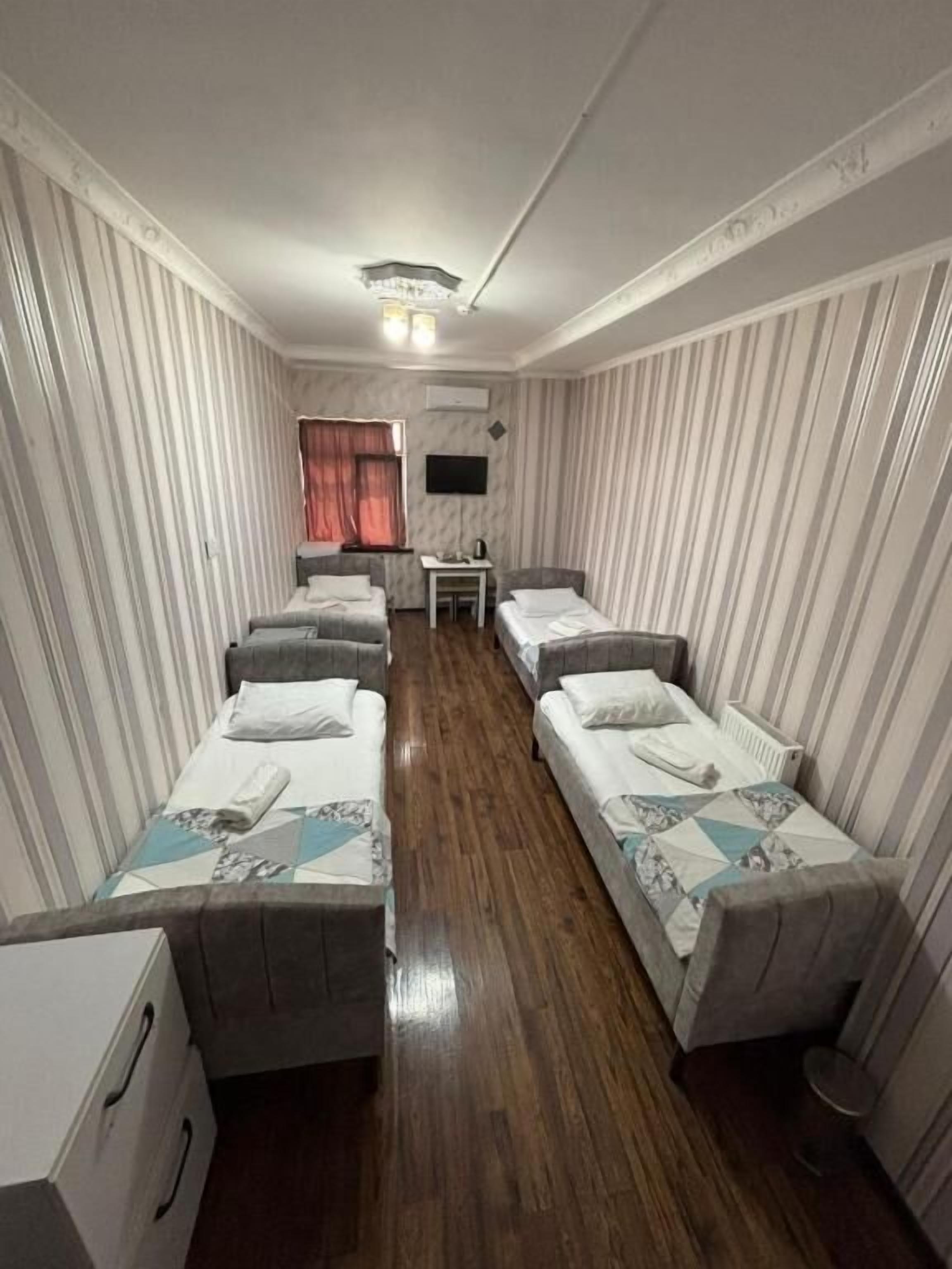 A hotel room with four single beds, a small table, a TV, and a window with curtains.