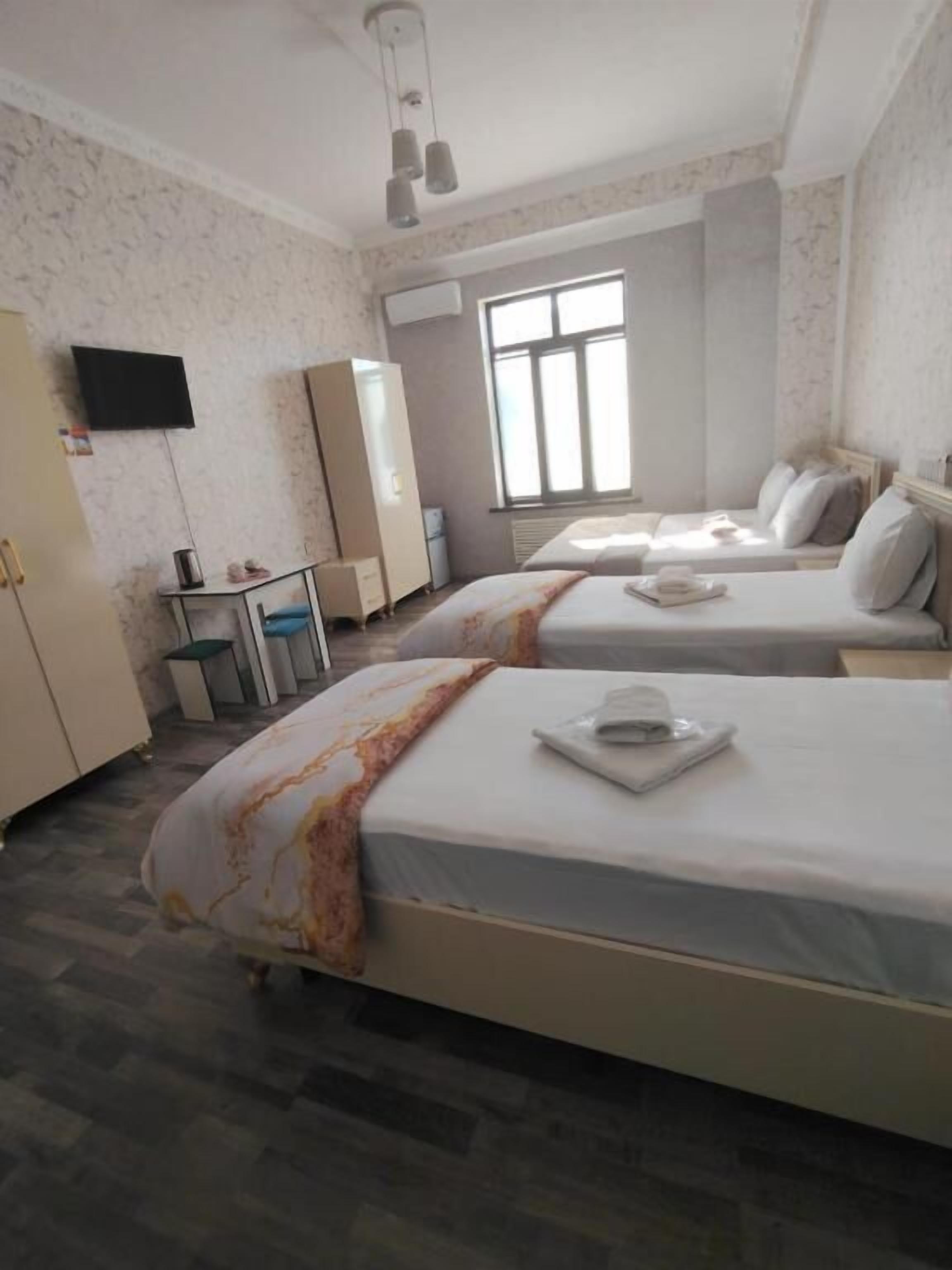 A hotel room with two beds, a wardrobe, a desk, a television, and a window.