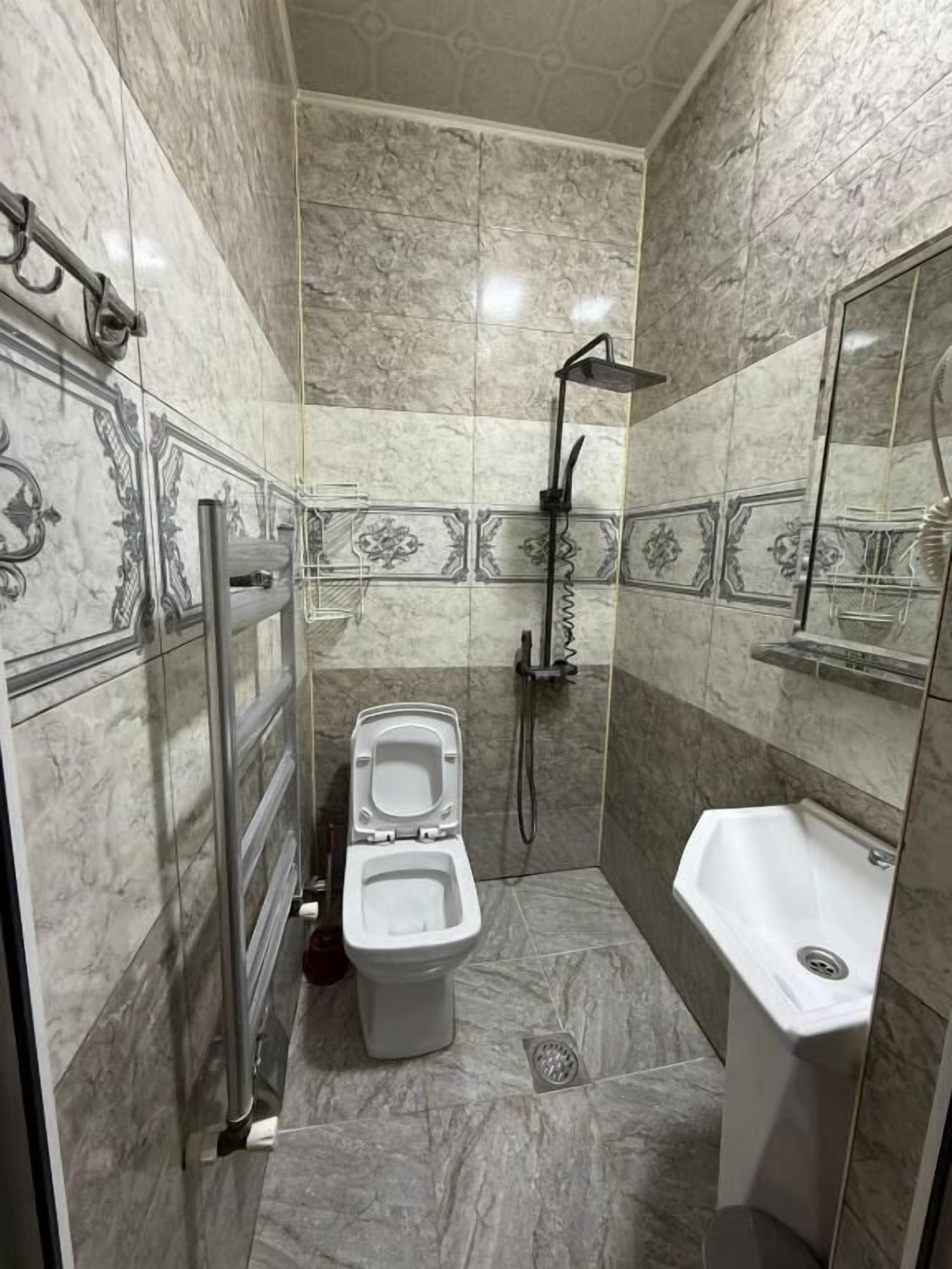 Un baño con inodoro, ducha, lavamanos y barra de apoyo.