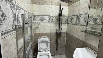 Un baño con inodoro, ducha, lavamanos y barra de apoyo.