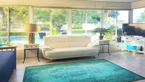 A modern living room with a white sofa, a blue couch, a green rug, and a TV on a white stand. - SALTWATER SMILES 3/2-HEATED POOL HOME 5 MILES FROM AMI WITH GAMES AND PING PONG. (BRADENTON,)