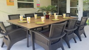 A dining table set with wicker chairs, a potted plant, and orange-patterned napkins. - SALTWATER SMILES 3/2-HEATED POOL HOME 5 MILES FROM AMI WITH GAMES AND PING PONG. (BRADENTON,)
