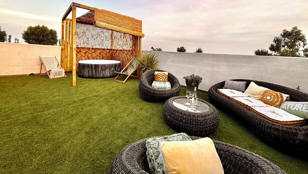 Une terrasse sur le toit agrémentée d’une pergola en bois, d’un jacuzzi, de meubles en osier et offrant une vue sur la mer.