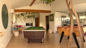 Un espace intérieur accueillant, équipé d’une table de billard, d’un baby-foot et d’un téléviseur.