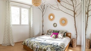 Une chambre à coucher comprenant un lit, une fenêtre et des éléments de décoration murale, notamment des miroirs et des branches d’arbres.