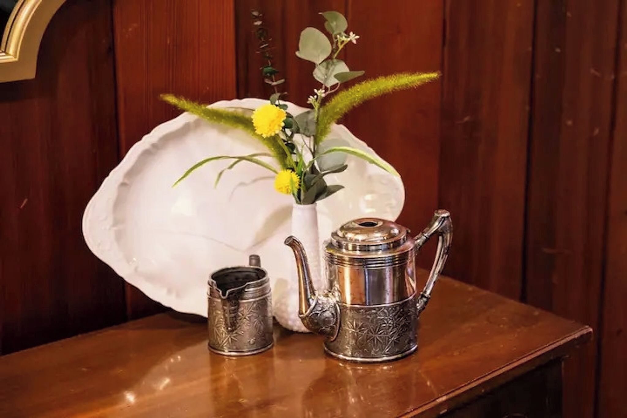 Un plato de cerámica blanca, una tetera de plata y una taza de plata sobre una mesa de madera.