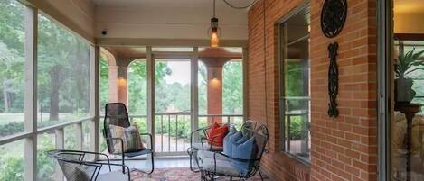 A covered porch with two metal chairs, a patterned rug, and a brick wall.