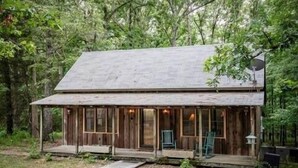 A rustic cabin with a porch, surrounded by dense forest. - The Lil' Sipp, 2BR Cabin by Velvet Ditch Villas (Oxford)